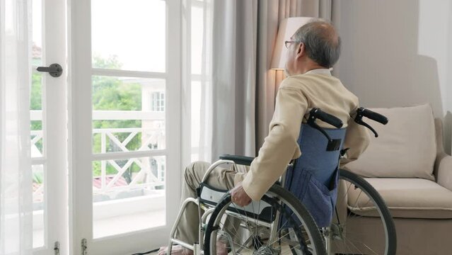 Lonely older thoughtful sad old man look outside windows in bedroom at retirement home, Asian senior man disabled feel depressed lonely sitting alone in wheelchair looking through window at hospital