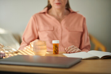 Mature businesswoman taking pills with cup of water when sitting at office desk