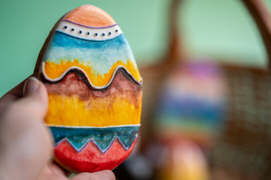 mano sosteniendo galleta en forma de huevo de pascua decorado a mano con fondo desenfocado