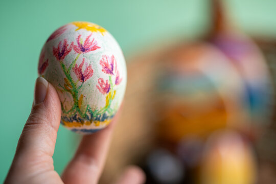 mano sosteniendo huevo de pascua decorado a mano con fondo desenfocado de canasta 