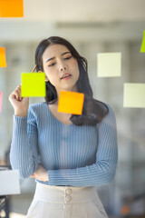 Happy asian businesswoman planning new project with sticky note in a creative writing on blank office glass