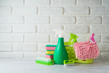 Eco friendly green cleaning bottles and supplies on white wooden table over brick wall background