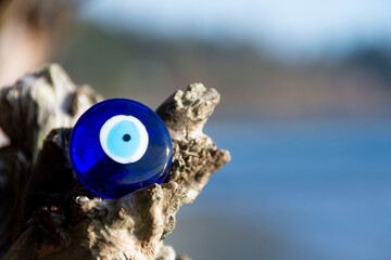 A close up image of a protective evil eye resting on driftwood with a ocean background.