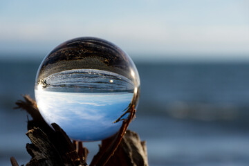 An image of a glass lens ball reflecting the inverted image of the blue Pacific Ocean and rocky...