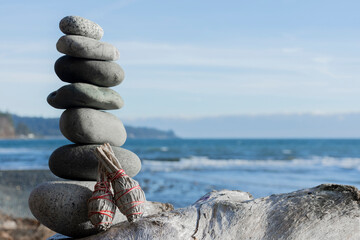 A tranquil image of stacked zen stones with two white sage smudge sticks and the blue Pacific Ocean in the background.