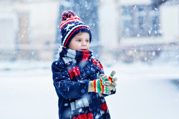 Cute little funny child in colorful winter fashion clothes having fun and playing with snow,...