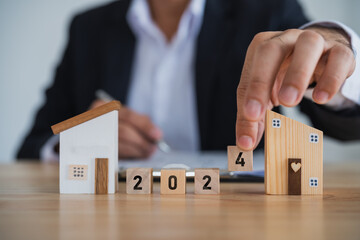 2024 new year target home loan trends. Businessman hold model house and wood blocks word LOAN. plan finances investments and savings to buy house real estate. Home accounting and tax and insurance. - obrazy, fototapety, plakaty