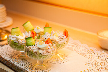 The photograph showcases an elegant food presentation with individual glass bowls filled with a fresh, colorful salad. The salad comprises crisp cucumbers, ripe tomatoes, and possibly some feta cheese