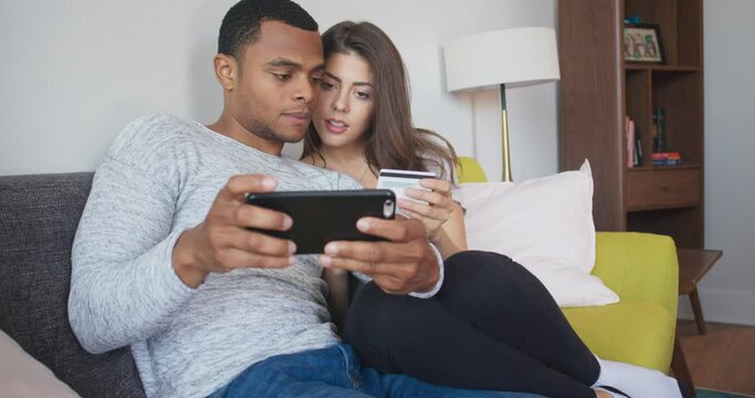 Young couple making online purchase together using credit card and smartphone. Millennial African American and Caucasian newlyweds booking vacation. 4k slow motion handheld