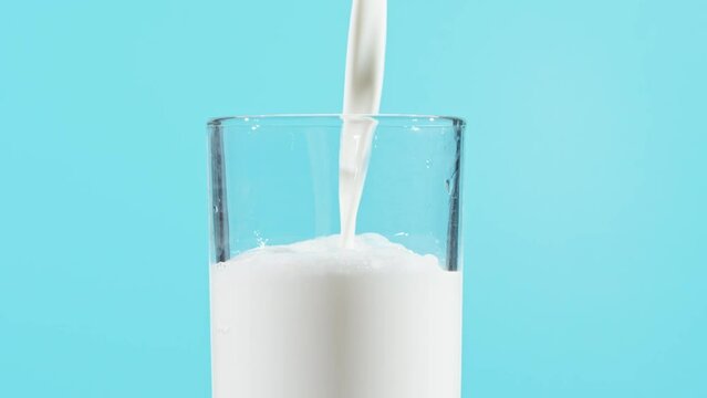 Slow motion of milk drink pouring into glass on blue background