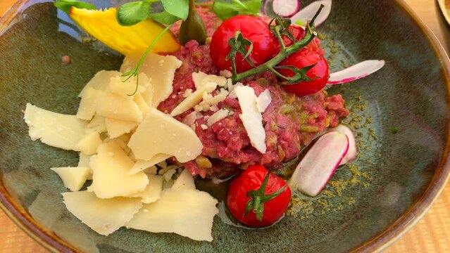 Delicious steak tartare with parmesan cheese, cherry tomatoes and capres on a plate, 4K shot