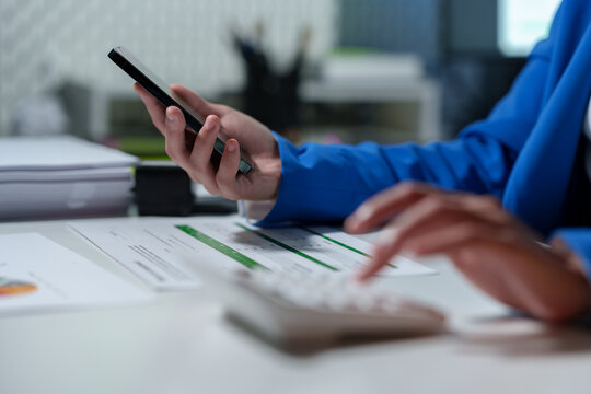 Young Asian business woman uses computing concept with calculator to calculate business principles. Work graph paper placed on table, accounting statistics concept at office.