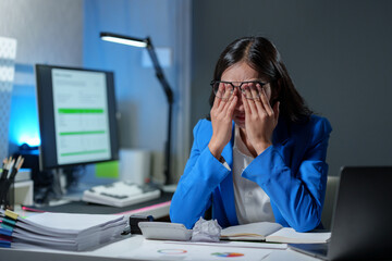 Asian businesswoman holding glasses has fatigue, headache, drowsiness, and boredom from sitting at a desk for a long time. Troubled financial paperwork and office syndrome symptoms.