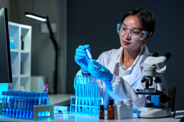 Fototapeta premium Medical scientist, researcher, lab assistant holding test tube through blue solution sample, doing chemical experiment and examining, comparing biological results, medical and research concept.