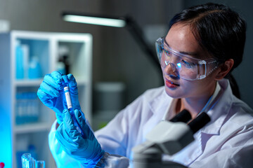 Medical scientist, researcher, lab assistant holding test tube through blue solution sample, doing...