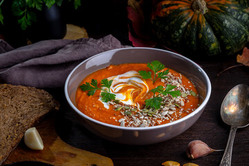 Pumpkin cream soup with sesame seeds, sunflower seeds and yogurt on a dark table.