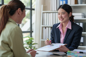 Two Asian businesswomen talk, consult, discuss work with presentation of project ideas, growth analysis, marketing and investment plans, data from charts in organization in office.
