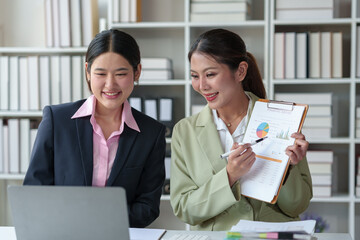 Two confident Asian businesswomen discuss and present ideas via laptop online on new project to analyze joint planning, financial statistics and investment market at office.