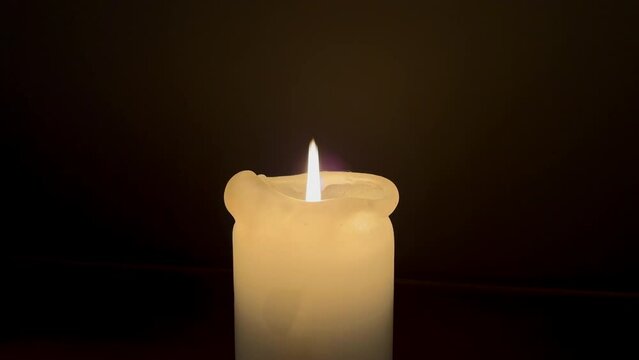 close up single candle flame lights burning in front of dark background - power outage, electricity switch off.
