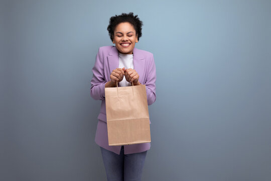 young positive successful latin business woman with ponytail hairstyle dressed in a jacket holds out a delivery package made of eco-friendly material