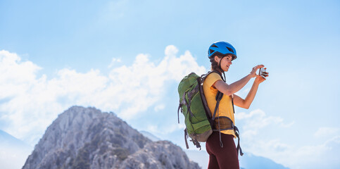 climber on top of the mountain takes a photo. Girl with a backpack and hard hat in the mountains....