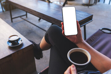 Mockup image of a woman holding mobile phone with blank desktop screen while drinking coffee in cafe - obrazy, fototapety, plakaty