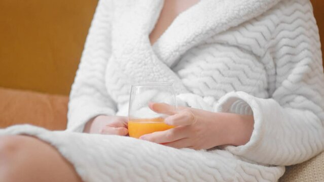 Gorgeous woman in white bathrobe relaxing on couch with glass of juice