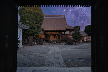 門の入り口から見える、大きな瓦屋根のお寺と境内の夜の風景 - obrazy, fototapety, plakaty