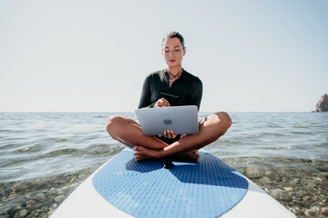 Digital nomad, freelancer, laptop. Happy smiling woman working on sup board at calm sea beach,...