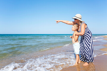 An elderly woman and a boy are standing on the seashore. A grandmother in a long striped dress and...