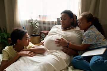 African American pregnant mom talking to her daughters during leisure time at home