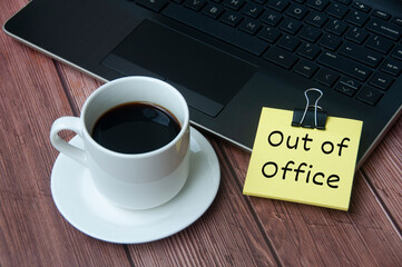 Coffee cup and laptop on wooden table with yellow notepad with text - Out of office.