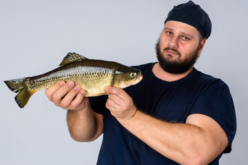 man with fish. a brutal bearded plump man in dark blue clothes stands on a gray background with a large river fish