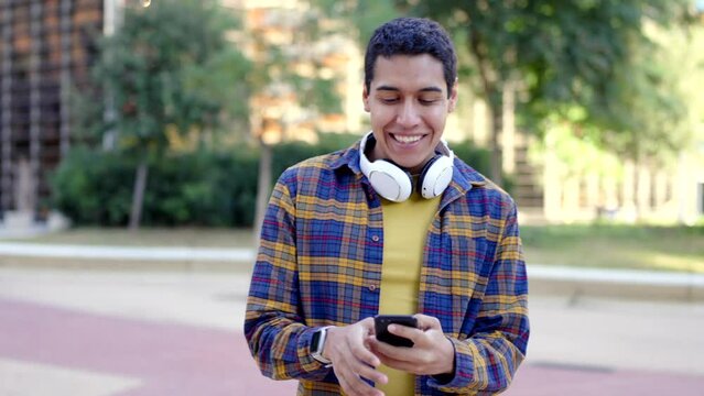Horizontal video with slow motion of a happy hispanic young man using phone in the street