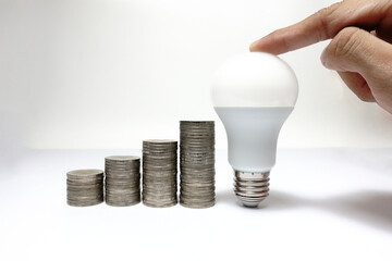 Finger touch on LED Light bulb with increasing piles of coins on white background,Business growth and finance.Coins graph-Financial plan-Business success-Business idea-opportunity concept.
