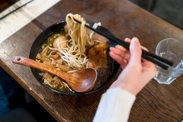 Woman using chopsticks to eat a ramen soup