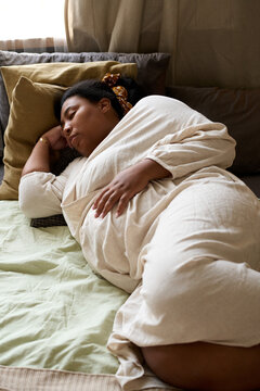 Vertical image of African American pregnant woman sleeping on bed in bedroom