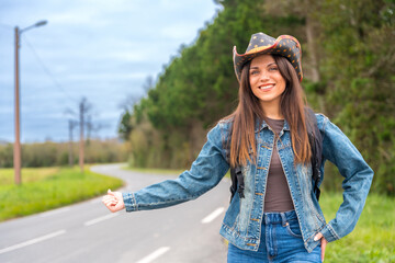 Woman in denim and cowboy hat hitchhiking