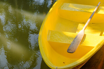 Wooden oar on yellow fiber rowboat in pond