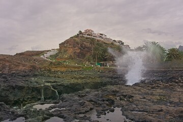 Agaete, Gran Canaria, Spain: Waves crashing the shore during bad weather conditions against a house on the top of the cliff