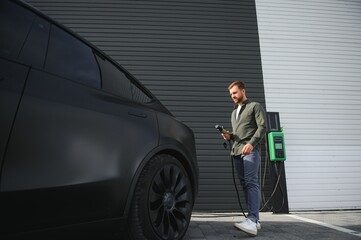 A man stands near a charging station and charges his electric car