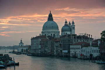 Light orange and pink sunset reflected in the water in Venice, with clear cityscape and...