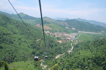The cable car is very high and distant, overlooking the forest and green trees. And you can still see villages and cities