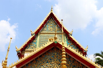 Double isosceles  triangle shape gable and roof of Buddhism church and blue sky background, Thailand. Thai native traditional art decorate on gable in golden, blue, red color.
