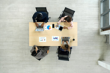 A team of workers is seated together at a big table in an office, sharing thoughts and talking. Top...