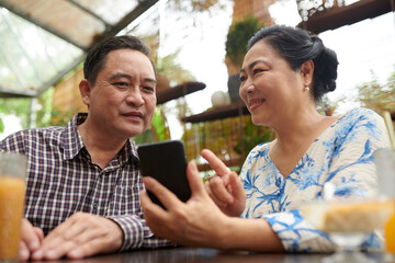 Smiling senior woman showing photo on social media to husband when they are spending time in coffeeshop
