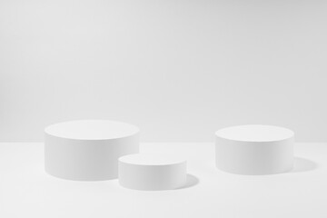 Abstract three white round podiums for cosmetic products in hard light, mockup on white background. Scene for presentation products, gifts, goods, advertising, design, sale, display in minimal style.