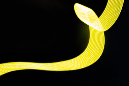 Yellow neon flowing wave of light as trail with smooth stripes on black background. Abstract background with motion light effect, light painting in disco style.