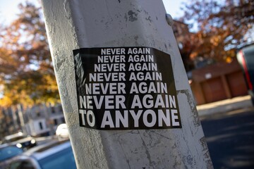 Poster with the phrase 'Never Again To Anyone' in white lettering in the Brooklyn