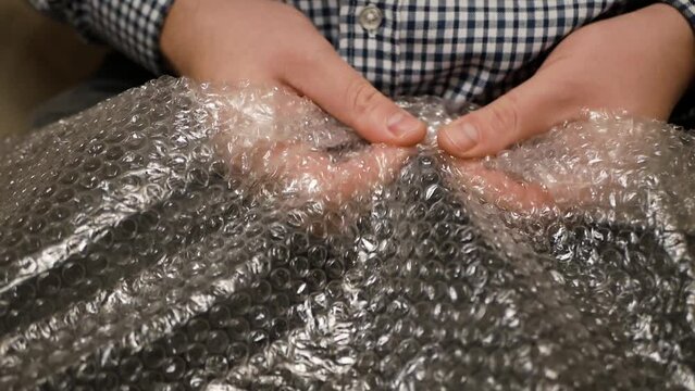 Fingers popping bubbles in bubble wrap close-up anti-stress therapy. Nervous man press plastic bubble wrap as a stress relief. man close up pressing bubble wrap with fingers from delivery packaging.